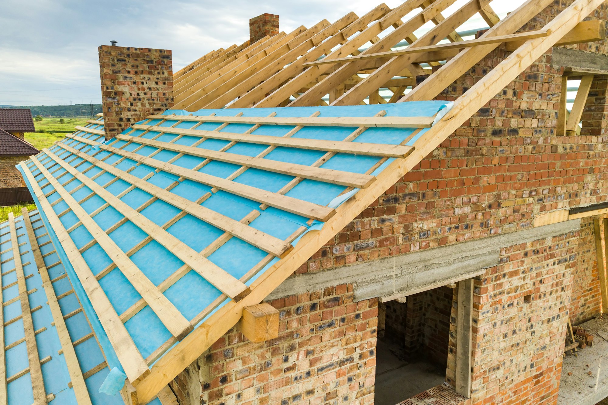 Aerial view of a brick house with wooden roof frame under construction