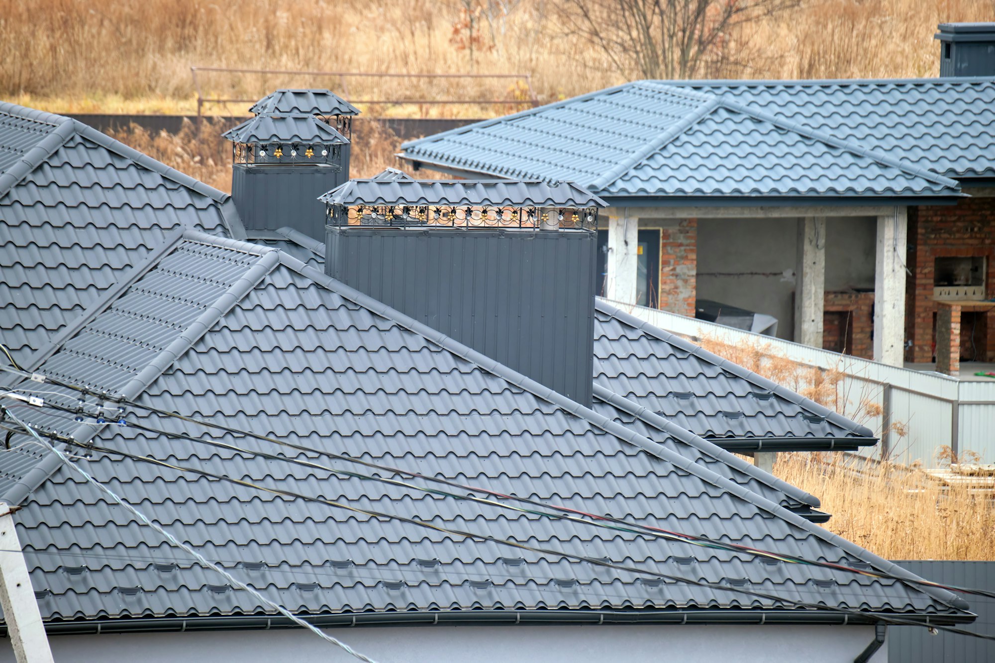 Chimney on house roof top covered with metallic shingles under construction. Tiled covering of